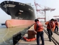 20 janvier 2014, port de Qingdao, province du Liaoning, nord-est de la Chine: des ouvriers préparent l’accostage d’un navire porte-conteneurs.