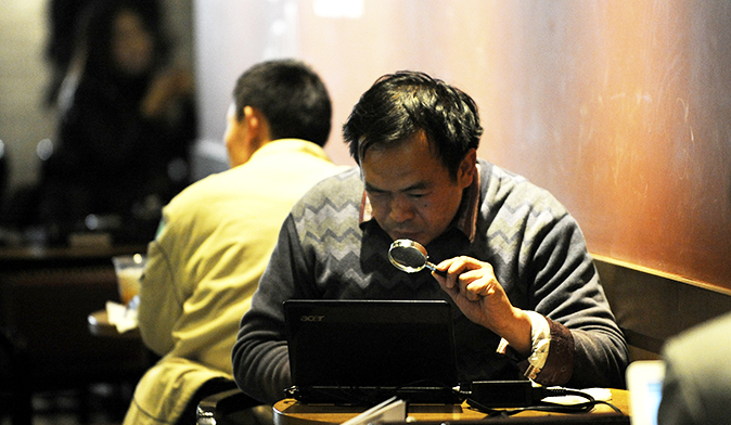 Un homme regarde son ordinateur portable avec une loupe dans un café de Pékin. Une nouvelle loi chinoise sur la Sécurité Nationale va renforcer la gestion du Web et et mettre en place des mesures plus draconiennes contre les attaques en ligne, les vols de secrets et la diffusion d’informations illégales ou nuisibles. (Wang Zhao/AFP/Getty Images)