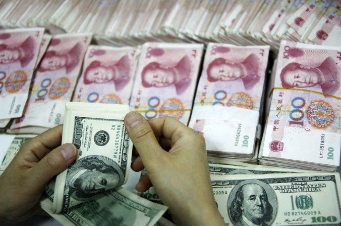 Billets de dollars comptés à côté des piles de billets de 100 yuans chinois (RMB) dans une banque de Huaibei, province d'Anhui à l’est de la Chine, le 23 septembre 2014. (STR / AFP / Getty Images)