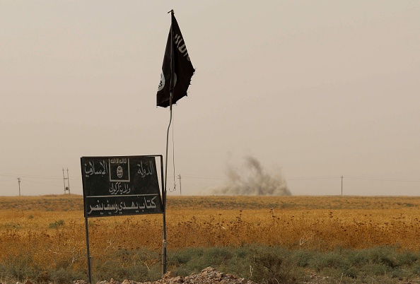 De la fumée monte au loin, derrière un drapeau du groupe terroriste ISIS 11 septembre 2015. (MARWAN IBRAHIM / AFP / Getty Images)