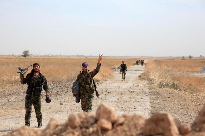 Des soldats du régime syrien font des signes alors qu’ils marchent sur une route dans une zone autour de l’aéroport militaire de Kweyris, dans la province orientale d’Alep, le 18 octobre 2015. (George Ourfalian/AFP/Getty Images)