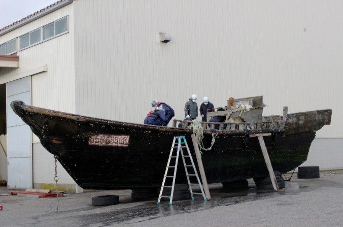 Cette photo prise le 24 novembre 2015 montre des enquêteurs des gardes côtes qui inspectent un bateau en bois au port Fukui de la ville de Sakai, préfecture de Fukui, à l’Ouest du Japon. Le navire a été trouvé à la dérive au large de la côte de Fukui. Le Japon enquête sur une douzaine de bateaux suspects récemment trouvés à la dérive au large des côtes du pays. Certains ont été retrouvés avec des corps en décomposition à leurs bords d’après les autorités. Le 27 novembre des médias ont émis l’hypothèse qu'ils venaient de Corée du Nord. Au moins 11 cas de bateaux en bois - dont certains gravement endommagés - avec 20 corps à bord ont été signalés entre octobre et novembre. (JIJI PRESS / AFP / Getty Images)