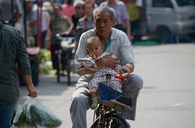 Un homme âgé tient un bébé dans ses bras en roulant sur le bord d'une route à Pékin le 8 septembre 2015. (Wang Zhao/AFP/Getty Images)