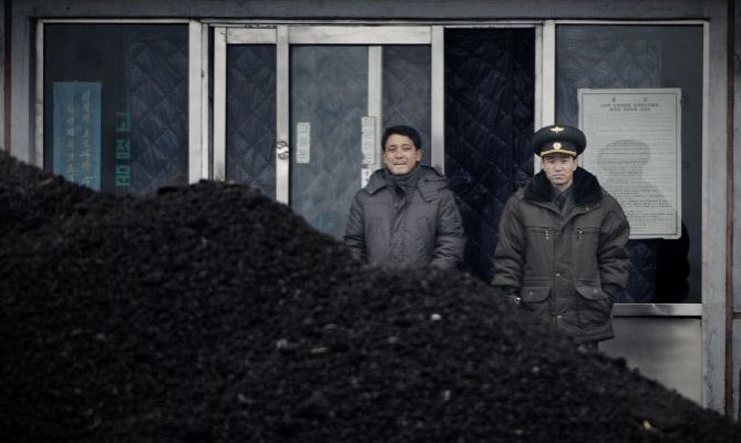 Un officier nord-coréen (d) avec un compatriote derrière un amas de charbon sur les rives du fleuve Yalu dans la ville frontalière nord-coréenne de Siniuju, le 14 décembre 2012. Le 18 février 2017, le ministère du Commerce chinois a annoncé la suspension des importations de charbon nord-coréen. (Wang Zhao / AFP / Getty Images)