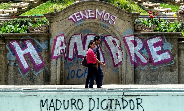 Un couple marche devant des graffitis disant « Nous avons faim » et « Maduro dictateur » le 8 aout à Caracas. Le dirigeant Nicolas Maduro n’est pas populaire. L’inflation est galopante et la nourriture et les médicaments manquent dans le pays. (RONALDO SCHEMIDT/AFP/Getty Images)
