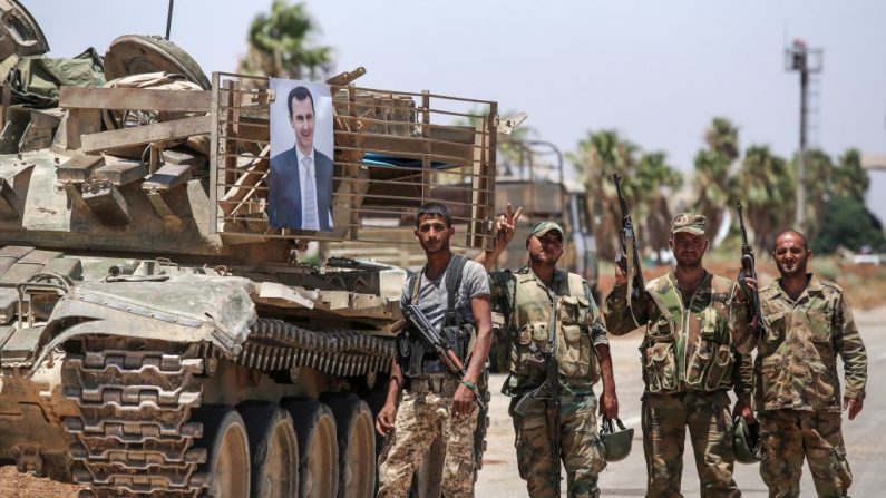   Des soldats du gouvernement syrien brandissent le geste de victoire à côté d'une photo du président syrien Bashar al-Assad accroché à un tank au poste frontière de Nassib avec la Jordanie dans la province de Daraa au sud juillet 2018.   Photo  YOUSSEF KARWASHAN/AFP/Getty Images.