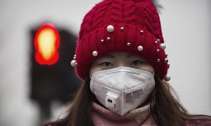 Une femme porte un masque pour se protéger contre la pollution alors qu'elle attend de traverser la rue dans un fort smog le 8 décembre 2015 à Pékin, en Chine. (Kevin Frayer/Getty Images)
