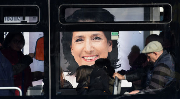 -Les voyageurs dans un bus passent devant une affiche électorale de la candidate à l'élection présidentielle Salomé Zurabichvili à Tbilissi le 27 novembre 2018, à la veille du second tour de l'élection présidentielle. Photo VANO SHLAMOV / AFP / Getty Images.