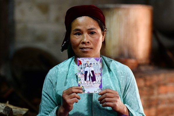 -Cette photo prise le 27 octobre 2018 montre Ly Thi My, une mère vietnamienne posant avec une photo de sa fille disparue Di chez elle à Meo Vac, une région frontalière montagneuse située entre la province vietnamienne de Ha Giang et la Chine. La plupart des habitants de cette partie du Vietnam ont une histoire sur le trafic de mariée. Photo de NHAC NGUYEN/AFP/Getty Images.
