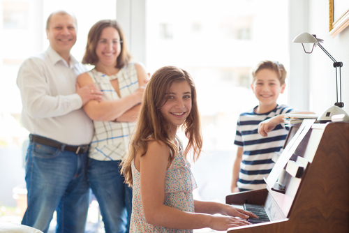 Une jeune famille heureuse écoute comment leur fille joue du piano à la maison. (Shutterstock)
