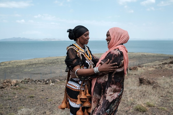 -La femme du gouverneur du comté de Marsabit en tenue tribale salue une femme au bord du lac Turkana, le plus grand lac désert du monde, dans le nord du Kenya, le 28 juin 2018. Les parcs nationaux du lac Turkana vont s’inscrire aux sites du patrimoine mondial en danger en raison, de menaces posées par un barrage éthiopien. Photo de Yasuyoshi CHIBA / AFP / Getty Images.