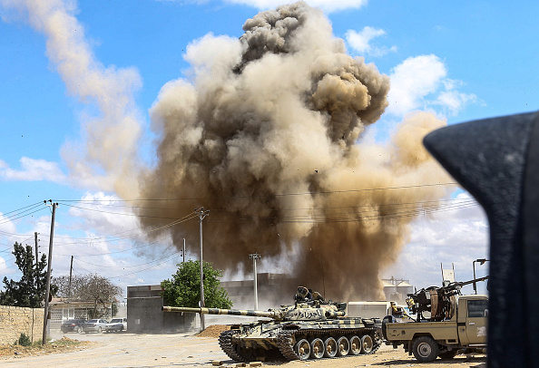 -Cette photo prise le 12 avril 2019 montre un nuage de fumée s'élevant d'une frappe aérienne derrière un char et des dispositifs techniques appartenant aux forces fidèles au gouvernement libyen lors des affrontements à Wadi. Rabie est situé à environ 30 kilomètres au sud de la capitale Tripoli. Photo de Mahmud TURKIA / AFP / Getty Images.