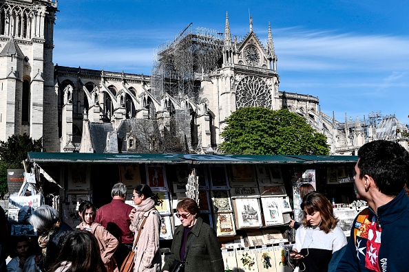 -Les gens passent devant une librairie traditionnelle « bouquiniste » le long de la Seine devant la cathédrale Notre-Dame de Paris le 17 avril 2019 dans le centre de Paris, deux jours après l’incendie qui a ravagé le chef-d'œuvre gothique vieux de 850 ans. Photo de STEPHANE DE SAKUTIN / AFP / Getty Images.