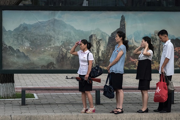 Sur cette photo prise le 29 juillet 2017, une femme tenant un fusil factice se tient à un arrêt de bus à Pyongyang. La Corée du Nord a déclaré le 30 juillet, que son dernier test ICBM était un "avertissement" visant les États-Unis pour leurs efforts visant à imposer de nouvelles sanctions à Pyongyang. Photo ED JONES / AFP / Getty Images.