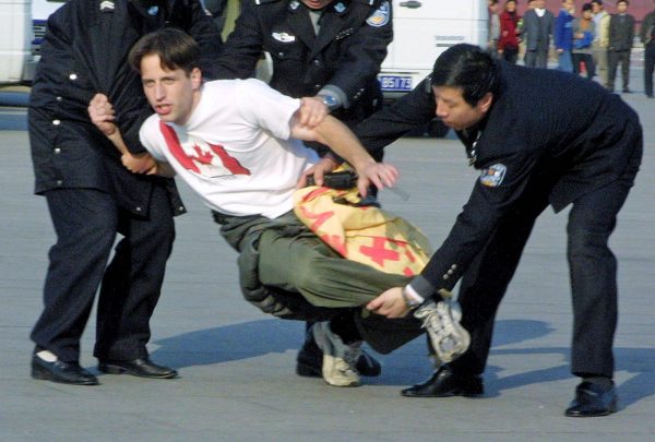 Deux, trois policiers chinois arrêtent un pratiquant de Falun Gong sur la place Tiananmen à Pékin. (Epoch Times /FLG)