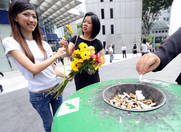 -Une militante remet des fleurs aux femmes de la rue pour les encourager à cesser de fumer, tandis qu'une fumeuse éteint sa cigarette à la poubelle à Singapour le 17 mars 2008. L'événement était organisé par le conseil de promotion de la santé de Singapour. Photo ROSLAN RAHMAN / AFP / Getty Images.