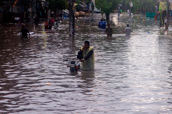 -Un Pakistanais parle au téléphone alors qu'il pousse son vélo dans une rue inondée après les fortes pluies de mousson à Lahore le 16 juillet 2019. Des pluies diluviennes ont provoqué des inondations subites et endommagé plus de 120 maisons et 30 magasins, et ont paralysé les approvisionnements en eau et en électricité. Photo par ARIF ALI / AFP / Getty Images.