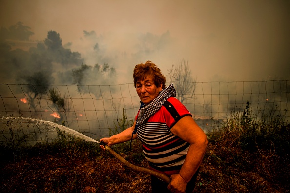 -Une villageoise utilise un tuyau d'arrosage pour éteindre les flammes lors d'un incendie de forêt dans le village de Roda à Macao, dans le centre du Portugal le 21 juillet 2019. Des avions et des hélicoptères se sont joints à près de 2 000 pompiers dans le centre du Portugal pour lutter contre d'énormes incendies. Photo de PATRICIA DE MELO MOREIRA / AFP / Getty Images.