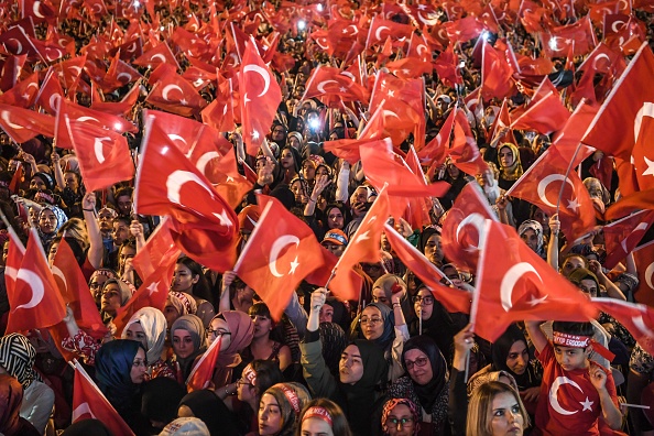 -L’année passée le 15 juillet 2018, à Istanbul, les gens agitent des drapeaux nationaux turcs devant le "Pont des Byrporus". La Turquie a commémoré le deuxième anniversaire d'une tentative de coup d'État sanglante suivie d'une série de purges dans le secteur public. Photo par OZAN KOSE / AFP / Getty Images.