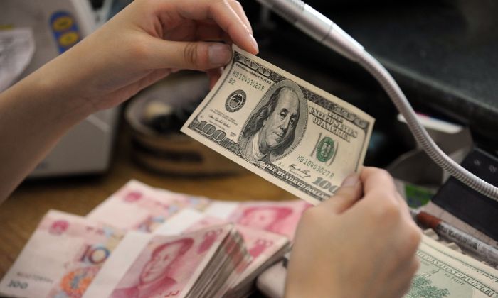 Un employé de banque chinoise vérifie un billet de 100 dollars ainsi que des piles de billets de 100 yuans à un comptoir bancaire de la ville de Hefei, province chinoise d'Anhui, le 30 septembre 2010. (STR/AFP/Getty Images)