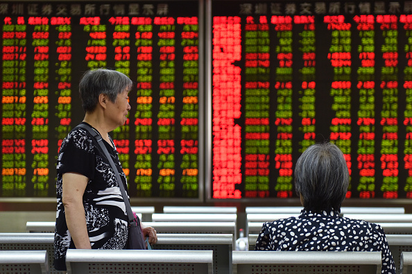 -Des femmes discutent devant un écran montrant les cours des actions d'une société de valeurs mobilières à Pékin le 5 août 2019. Les marchés asiatiques ont chuté le 5 août, le yuan chinois a fortement chuté. Photo par Greg Baker / AFP / Getty Images.