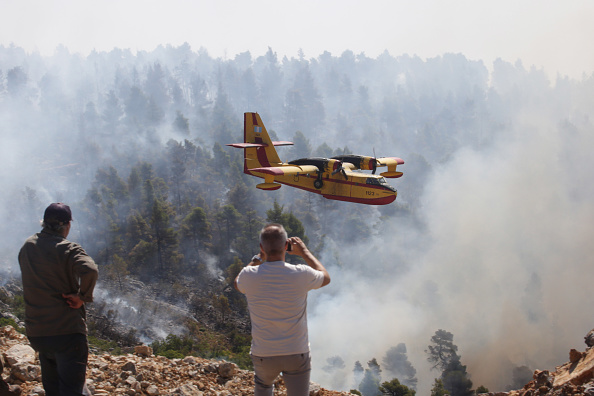 -Les gens regardent un avion de lutte contre les incendies un Canadair qui jette de l'eau sur un feu de forêt qui brûle près du village de Stavros le 14 août 2019 à Evia, en Grèce. L'état d'urgence a été déclaré sur l'île d'Eubée et plusieurs villages ont été évacués, déplaçant des centaines d'habitants alors que les pompiers tentent de maîtriser les incendies de forêt. Photo de Milos Bicanski / Getty Images.