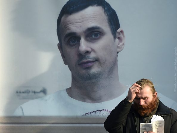-Un homme prie devant l’affiche représentant le réalisateur ukrainien Oleg Sentsov emprisonné dans une prison russe. Photo de Sergei SUPINSKY / AFP / Getty Images.