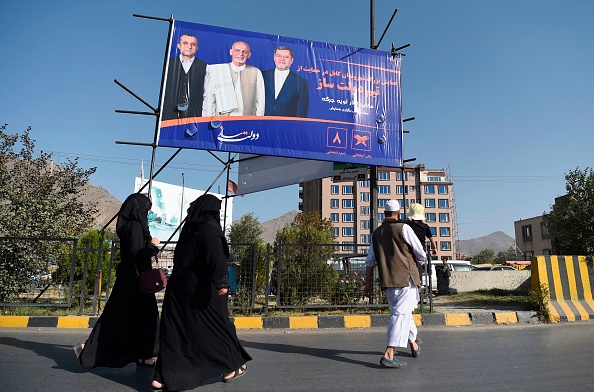 Des résidents marchent devant un panneau d'affichage avec une affiche du candidat à la présidence afghane et président sortant de l'Afghanistan, Ashraf Ghani, campagne pour la présidentielle à Kaboul le 11 septembre 2019. Photo de WAKIL KOHSAR / AFP / Getty Images.