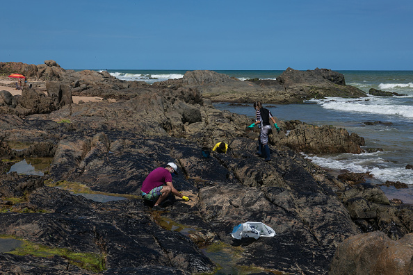 -Des volontaires enlèvent du pétrole sur des rochers sur la plage de Pedra do Sal, à Salvador, dans l'État de Bahia, au Brésil, le 19 octobre 2019. Un énorme déversement de pétrole au large de la côte nord-est du Brésil, a taché plus de 130 plages, pourrait être dû à un "navire fantôme" transportant Le pétrole vénézuélien en violation des sanctions américaines, a déclaré un expert proche de l'enquête sur la catastrophe. Photo ANTONELLO VENERI / AFP via Getty Images.