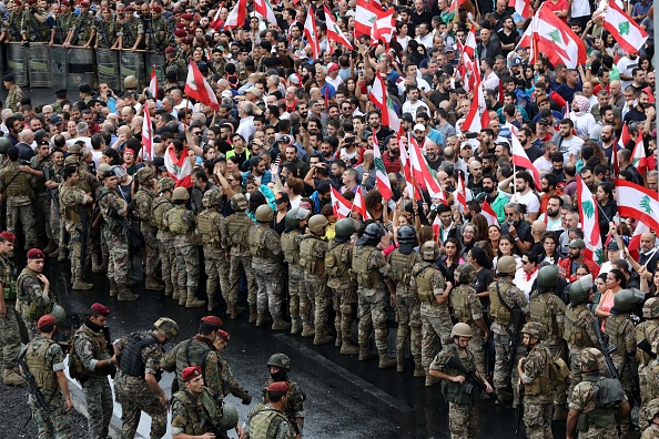 -Des manifestants antigouvernementaux confrontés à des soldats de l'armée libanaise agitent des drapeaux nationaux dans la région de Jal al-Dib, dans la banlieue nord de Beyrouth, la capitale libanaise, le 23 octobre 2019. Les manifestations déclenchées le 17 octobre par un projet de taxe sur WhatsApp et d'autres applications de messagerie se sont transformées en une mobilisation intersectorielle sans précédent dans la rue contre la classe politique. Photo par ANWAR AMRO / AFP via Getty Images.