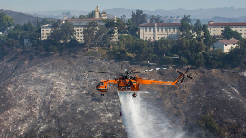 Un hélicoptère fait tomber de l'eau sur des maisons alors que l'incendie Getty brûle dans la région de Brentwood, en Californie, le 28 octobre 2019. (APU GOMES/AFP via Getty Images)