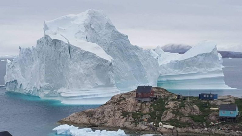 Un iceberg derrière des maisons et des bâtiments à l'extérieur du village d'Innarsuit, une île située dans la municipalité d'Avannaata, dans le nord-ouest du Groenland. (Magnus Kristensen / AFP / Getty Images)