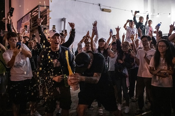 -Un partisan favorable à la démocratie ouvre une bouteille de champagne devant un bureau de vote pour célébrer le 25 novembre 2019, après la perte du siège du candidat pro-Pékin, aux élections du conseil de district de Tuen Mun à Hong Kong, Hong Kong. Photo de PHILIP FONG / AFP via Getty Images.