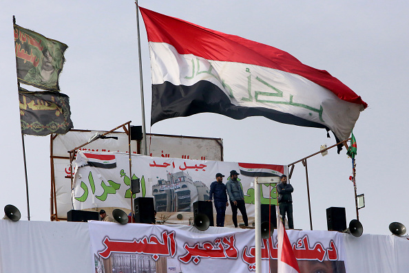 -Les Irakiens se rassemblent sur la place Tahrir dans la capitale Bagdad au milieu des manifestations anti-gouvernementales en cours le 10 décembre 2019. L'écriture arabe sur une bannière sous le drapeau national irakien se lit comme suit : "Votre vie est précieuse, ne traversez pas le pont". Photo par SABAH ARAR / AFP via Getty Images.