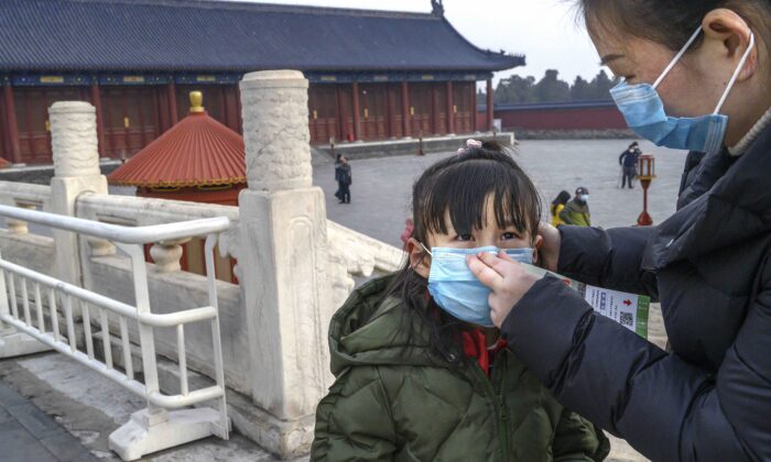 Une femme chinoise met un masque de protection sur une jeune fille alors qu'elle visite le Temple du Ciel à Pékin, en Chine, qui est resté ouvert pendant la fête du Nouvel An chinois et du Festival du printemps, le 27 janvier 2020. (Kevin Frayer/Getty Images)