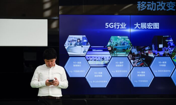 Un homme utilise son téléphone portable, devant un écran montrant l'industrie chinoise 5G, à l'extérieur d'un bureau de télécommunications à Pékin le 25 septembre 2019. (WANG ZHAO/AFP via Getty Images)