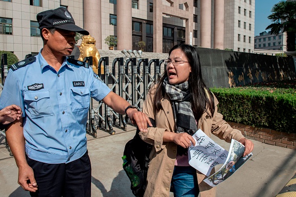 Cette photo prise le 31 octobre 2019 montre Xu Yan (à droite), épouse de l'avocat des droits de l'homme Yu Wensheng, tenant une feuille indiquant: "Je veux demander une rencontre avec le juge Liu Mingwei" et une photo de son mari. Le  personnel de sécurité (à gauche) lui demande de s'éloigner à l'extérieur du tribunal populaire de Xuzhou à Xuzhou. Xu, 37 ans, a voyagé une vingtaine de fois de Pékin à Xuzhou dans la province du Jiangsu dans une vaine lutte pour obtenir des informations sur son mari Yu Wensheng qui a été placé en garde à vue l'année dernière. (Photo : NICOLAS ASFOURI/AFP via Getty Images)