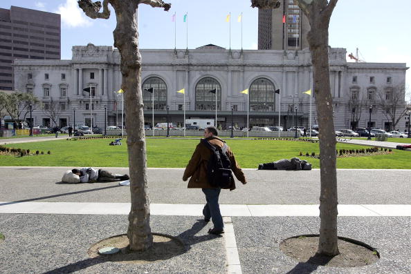 -Un homme passe devant deux sans-abris dormant dans le parc en face de la mairie de San Francisco Californie. Selon un rapport du Département du logement et du développement urbain, plus de 750 000 sans-abris vivent dans les rues, les abris et les logements de transition aux États-Unis. Photo de Justin Sullivan / Getty Images.
