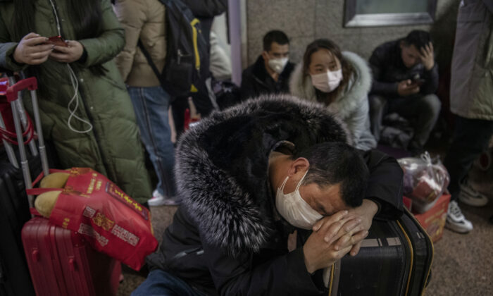 Un Chinois porte un masque de protection alors qu'il dort avant de monter à bord d'un train pour aller au Festival annuel du printemps dans une gare de Pékin, en Chine, le 23 janvier 2020. (Kevin Frayer/Getty Images)