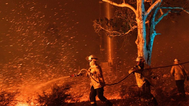 Cette image prise le 31 décembre 2019 montre des pompiers en train d’arroser les braises pour protéger les maisons avoisinantes contre les incendies près de la ville de Nowra, dans l'État australien de Nouvelle-Galles du Sud. (SAEED KHAN/AFP/Getty Images)