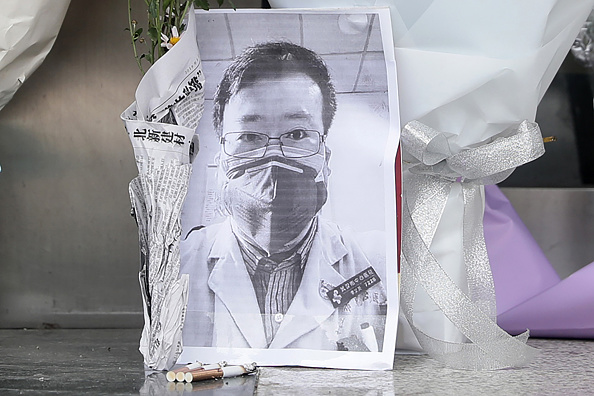 -Une photo de l'ophtalmologiste décédé Li Wenliang est vue avec des bouquets de fleurs à la succursale de Houhu de l'hôpital central de Wuhan, dans la province centrale du Hubei en Chine le 7 février 2020. Un médecin chinois qui a été puni après avoir sonné l'alarme au sujet du nouveau coronavirus chinois est décédé de l'agent pathogène le 7 février 2020. Photo par STR / AFP via Getty Images.