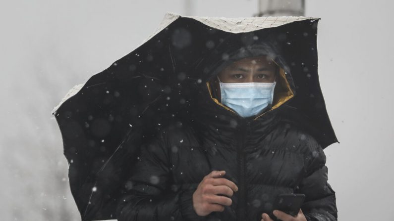 Un homme porte un masque de protection alors qu'il tient un parapluie sur le pont de la rivière Yangzi tandis que la neige tombe à Wuhan, Hubei, Chine, le 15 février 2020. (Getty Images)