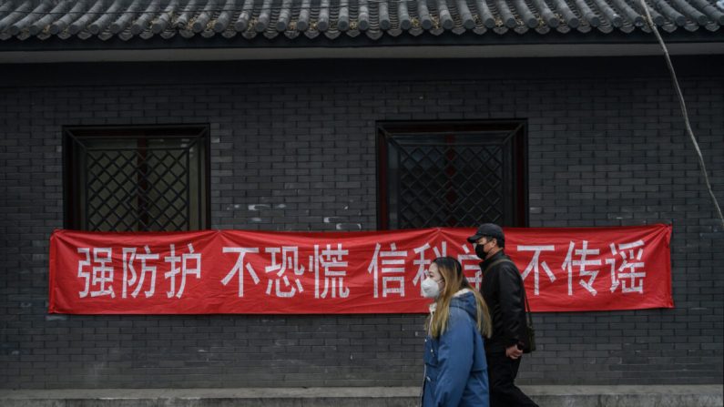 Des Chinois portant des masques de protection passent devant une banderole qui annonce : « Les mesures de prévention sont solides, ne paniquez pas, croyez en la science, ne répandez pas de rumeurs » dans un quartier résidentiel de Pékin, le 20 février 2020. (Kevin Frayer/Getty Images)
