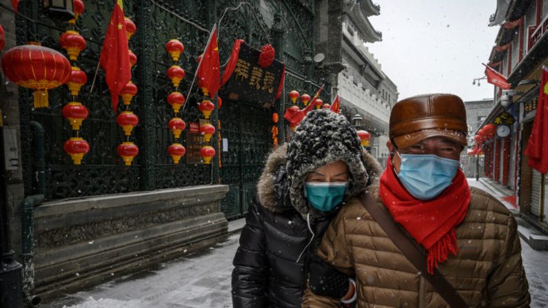 Un couple de Chinois porte des masques de protection alors qu'il marche sous la neige dans une rue commerciale vide et fermée à Pékin, en Chine, le 5 février 2020. (Kevin Frayer/Getty Images)
