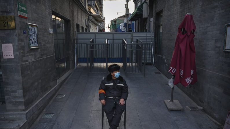 Un garde chinois porte un masque facial et observe une rue près d'une barricade qui bloque un quartier résidentiel d'une zone commerciale à Pékin, le 11 mars 2020. (Kevin Frayer/Getty Images)
