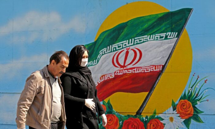 Des Iraniens masqués passent devant une peinture murale arborant leur drapeau national à Téhéran le 4 mars 2020. (Atta Kenare/AFP via Getty Images)