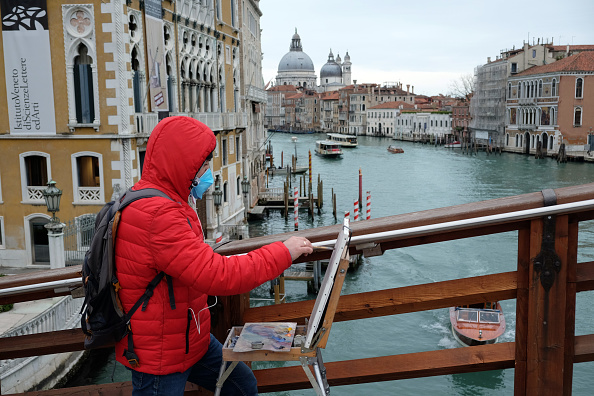 -Un homme portant un masque de protection sur le pont de l'Academia à Venise le 8 mars 2020 une vue sur le Grand Canal vide de bateaux avec l'église Salute à gauche. Photo par ANDREA PATTARO / AFP via Getty Images.
