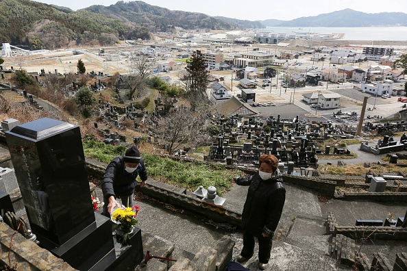 -Les gens déposent des fleurs sur les tombes de leurs proches dans un cimetière à Otsuchi, préfecture d'Iwate, le 11 mars 2020, à l'occasion du neuvième anniversaire de la catastrophe du tsunami de 2011. Les craintes concernant le nouveau coronavirus ont forcé une réduction des commémorations publiques. Photo par STR / JIJI PRESS / AFP via Getty Images.