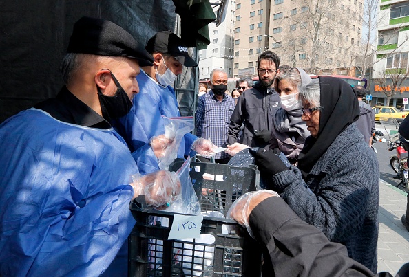 Des gens font la queue pour recevoir des colis de précautions contre le nouveau coronavirus fournis par une milice fidèle à la République islamique d'Iran. Photo de STRINGER / AFP via Getty Images.