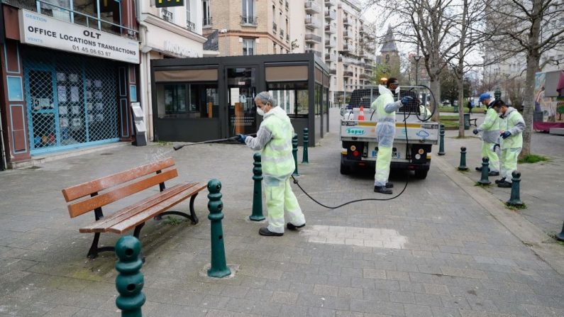 Les employés d'une entreprise de nettoyage pulvérisent du désinfectant sur le mobilier urbain dans une rue de Suresnes, près de Paris, le 18 mars 2020. (Photo par Thomas SAMSON / AFP) (Photo par THOMAS SAMSON/AFP via Getty Images)